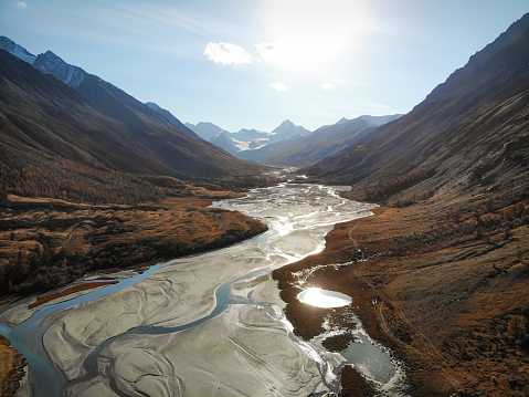 Amazing autumn evening aerial view with winding mountain river valley, glacier, scree, rocky road and golden trees captured from drone. Altai, Russia