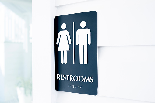 A close up of a unisex bathroom sign on a white wooden wall.