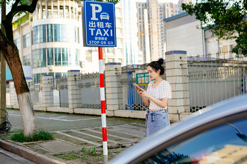 A young beautiful woman calls a taxi with her smartphone on the road