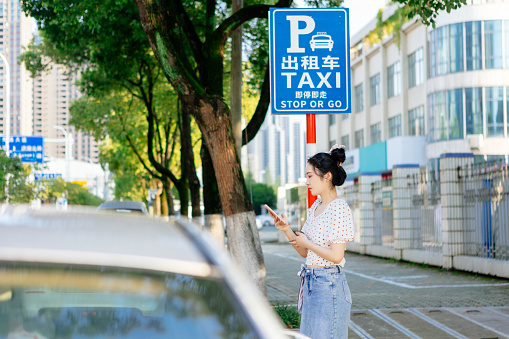 A young beautiful woman calls a taxi with her smartphone on the road