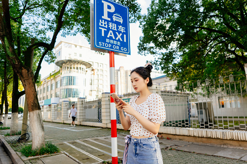 A young beautiful woman calls a taxi with her smartphone on the road