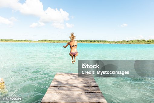 istock Happy young woman jumping from pier into beautiful lake 1430699064