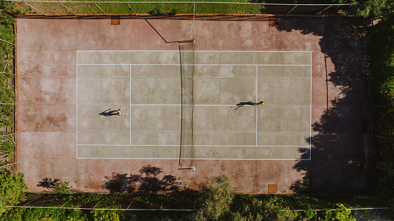 Drone point of view sport training Asian Indian female Tennis Player Serving The Ball practicing at tennis court directly above with coach guidance
