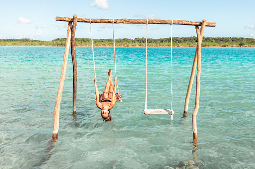 View of woman swinging on white sand beach relaxing and sunbathing by the lagoon in Mexico