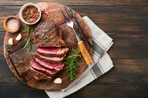 Steaks. Sliced grilled meat steak New York or Striploin with spices rosemary and pepper on black marble board on old wooden background. Top view. Mock up.