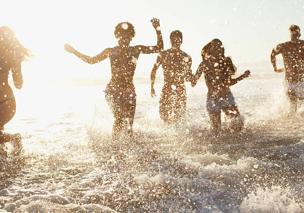 amigos jugando en las olas en la playa - wading fotografías e imágenes de stock