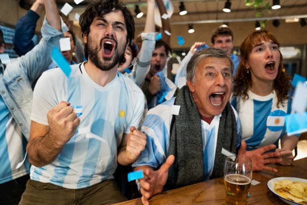 Argentine sports fans shouting and cheering for national team at sports bar Medium shot of group of Argentine sports fans shouting and cheering for national team at sports bar at night time chanting stock pictures, royalty-free photos & images