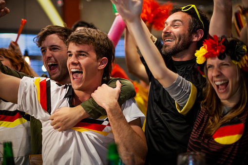 Mid shot of German football supporters shouting and celebrating at crowded sports bar after national team scores goal in an international game