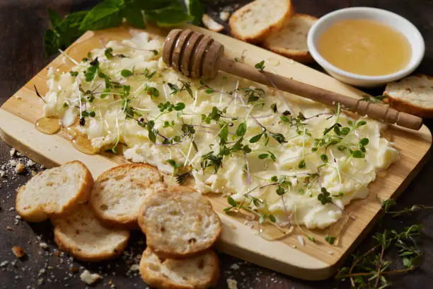 The Viral Butter Charcuterie Board with Fresh Herbs, Micro Greens, Organic Honey and Toasted Baguette Slices on a Bamboo Cutting Board