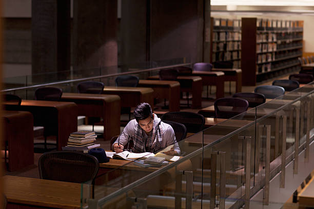 student working in library at night - üniversite stok fotoğraflar ve resimler
