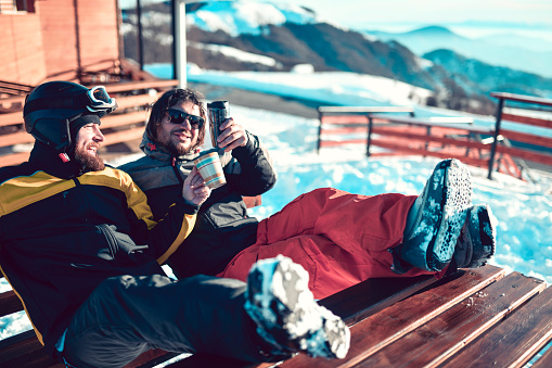 Fun Times For Male Friends Drinking Tea On Mountain Top After Getting Tired From Skiing