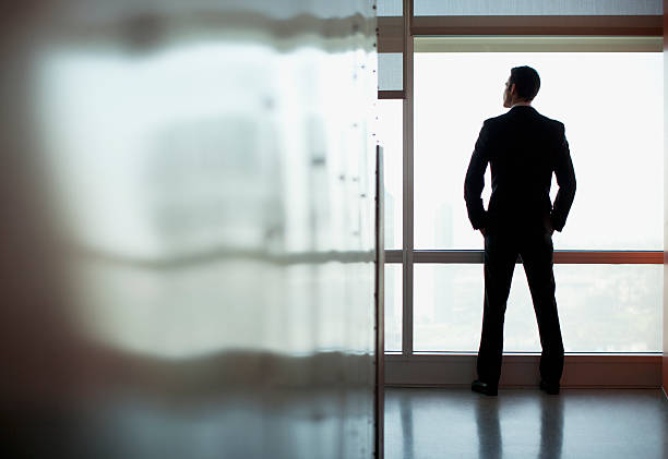 empresario mirando por la ventana de oficina - full length windows fotografías e imágenes de stock