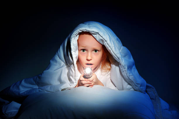 Little girl hiding under the blanket with a flashlight