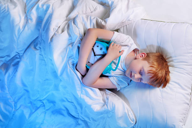 istock Top view of a boy in bed hugging blue clock 1430722546