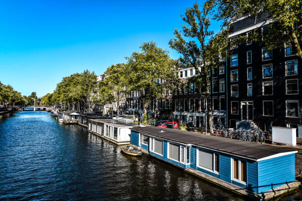 maisons de bateaux sur le canal de la rivière amstel à amsterdam, pays-bas - montelbaan tower photos et images de collection