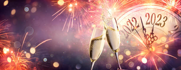 2023 New Year Eve Celebration With Champagne  - Countdown To Midnight - Clock Fireworks And Flutes On Abstract Defocused Background stock photo