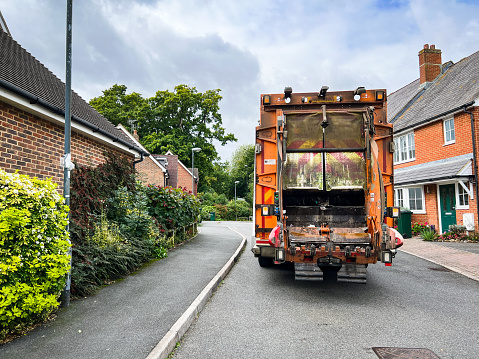 Rear view of a garbage truck on a residential street with modern red brick houses in southeast England.