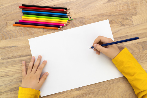 Child hands drawing with pencil on white paper, top view. Kids painting mock up.