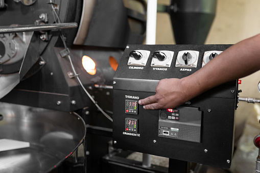 Close up of a man hand setting the buttons of a coffee roaster machine. Concept of local coffee production