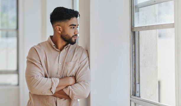 istock Serious businessman thinking about future, doubt and mindset while looking out of a window standing alone in an office at work. Latin man standing feeling worried, anxiety and idea about career 1430735868