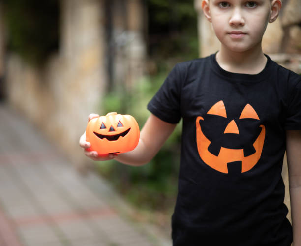 Cute kid boy in jack-o-lantern pumpkin t-shirt holding lantern in Halloween holiday. stock photo