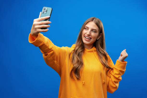 Photo of attractive young woman takes selfie photo on smartphone on blue background stock photo