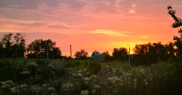 istock Bright beautiful orange sky at dawn over trees, a house and a grassy field 1430740177