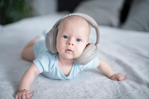 Funny portrait of cute baby boy with wireless headphones too big for his head.