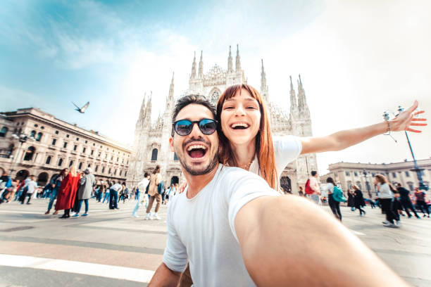 feliz pareja tomándose una selfie frente a la catedral del duomo en milán, lombardía - dos turistas divirtiéndose en románticas vacaciones de verano en italia - vacaciones y concepto de estilo de vida viajero - viaje fotografías e imágenes de stock