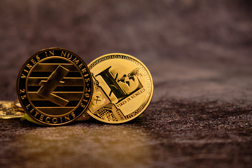 Close-up of the Litecoin Cryptocurrency with a golden reflection on the table and with an out of focus background.