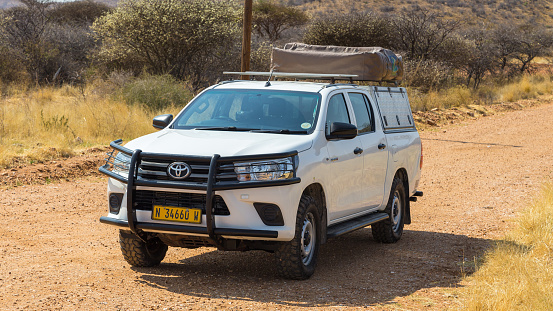 Windhoek, Namibia - 28 September 2018: Typical 4x4 rental car in Namibia equipped with camping gear and a roof tent driving on a dirt road through the Namibian wilderness.