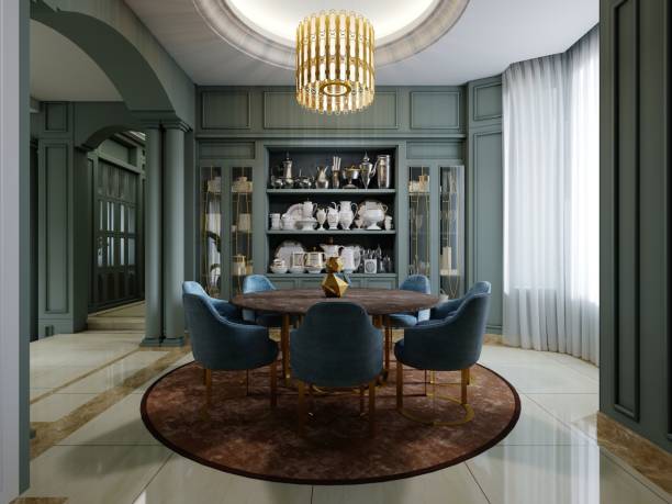 Dining room with a round table with blue chairs and a brown carpet in a green interior with shelves with crockery.