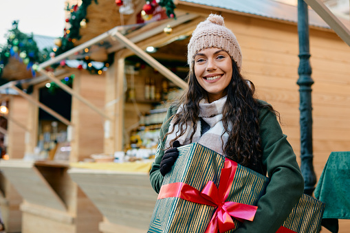 Happy woman with gift box enjoying at Christmas market and looking at camera.