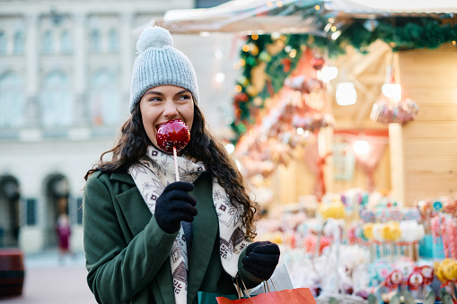 Young woman enjoying at Christmas fair while eating taffy apple.