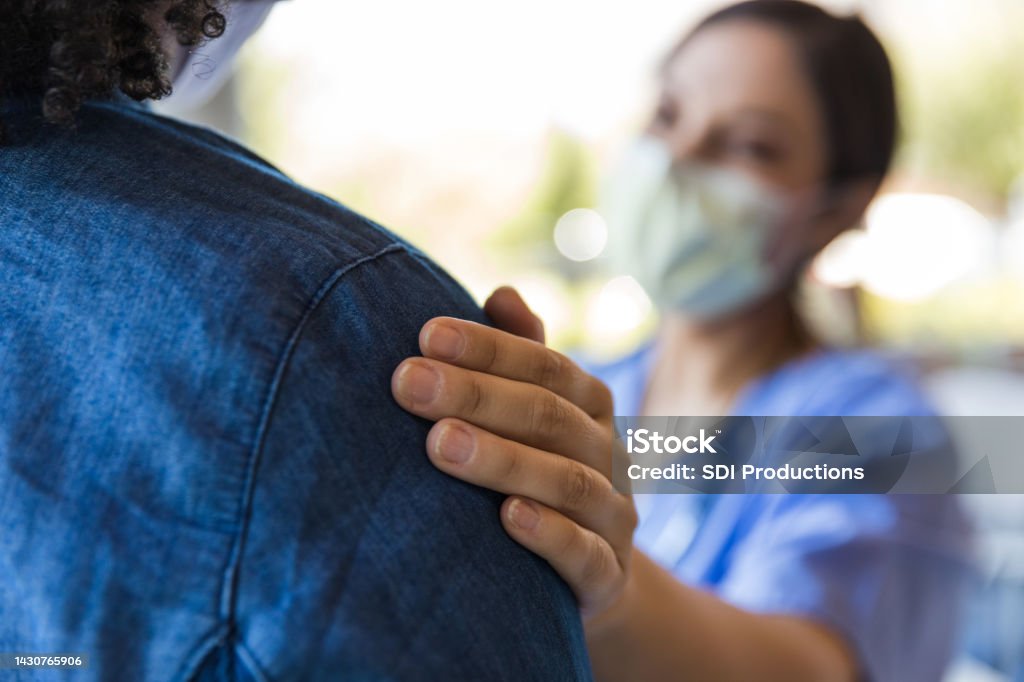 Doctor comforts a patient The doctor places her hand on the unrecognizeable person to comfort them while delivering difficult news. Patient Stock Photo