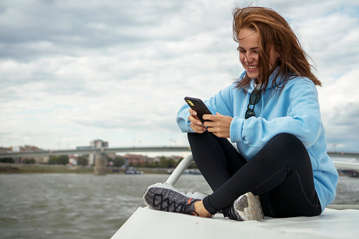 Woman sitting on the top deck of the boat using her mobile phone and smiling.