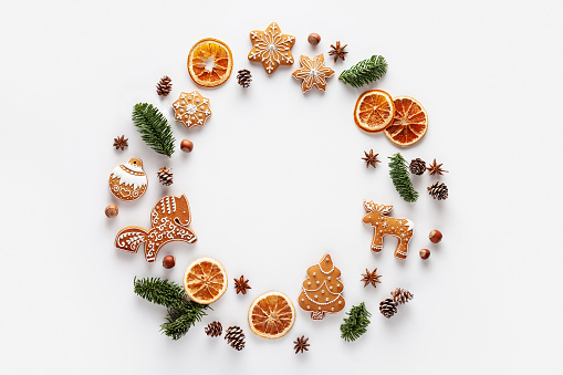 The frame is made of Christmas gingerbread, nuts, cones, dried orange slices and anise stars on a white background.
