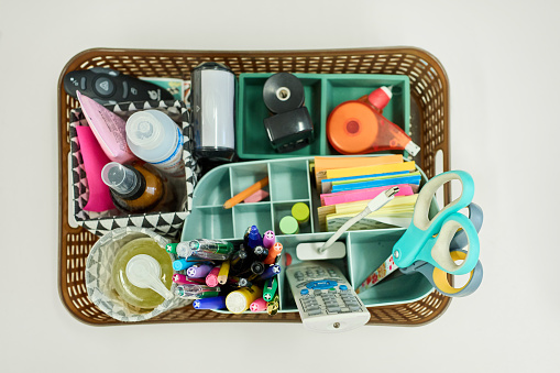 High angle view of a variety of school supplies sitting in a basket on a table in a classroom