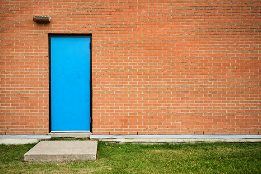 Blue door and step on a the red brick wall of a school building
