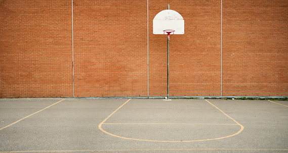 Basketball hoop and court in front of a the brick wall of a school with no students
