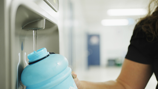 Close-up of a teacher filling her reusable bottle at a water fountain in the hallway of a school