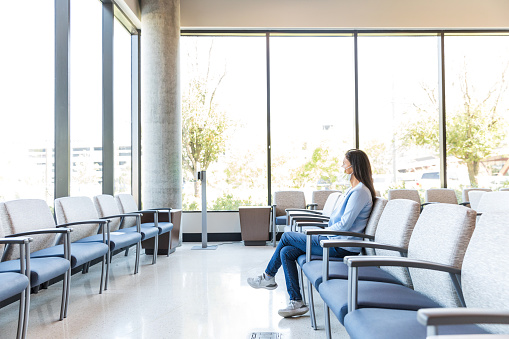 The adult female patient sits in the waiting room of the medical clinic alone.