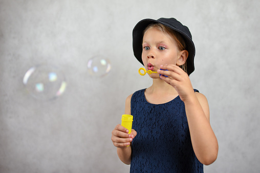 Young girl in a hat and dress blows bubbles.