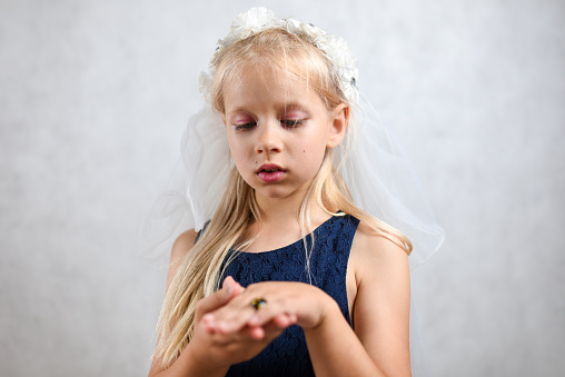 A child with a white veil is wearing a wedding ring.