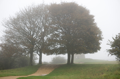 Looking over a Cotswold stone wall towards the historic Broadway Tower in a foggy morning, which sits high on the Cotswold escarpment at 1024 feet (312m) above sea level. The second highest after Cleeve Hill