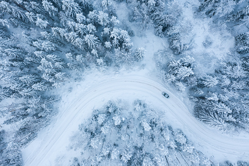 Car on a sharp turn of a winter road in a snow-covered forest top view.