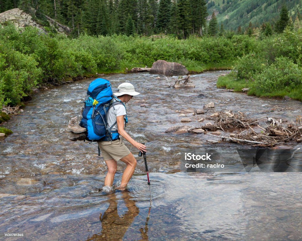 Mature backpacking woman crossing a river. Four Pass backpacking trip around the Maroon Bells. Aspen, Colorado. Active Lifestyle Stock Photo