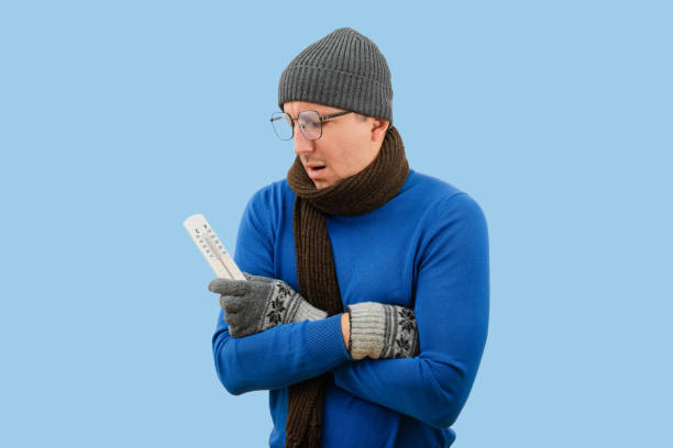 portrait d’hiver d’un homme regardant dans un thermomètre sur un fond bleu isolé. saison froide d’hiver - thermometer cold fever focus photos et images de collection