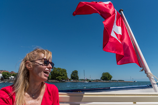 Mature blonde woman with glasses laughing and swiss flag fluttering on the aft of a boat on lake Leman.