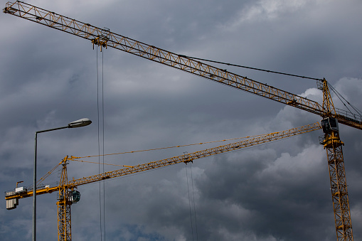 Two Cranes on Construction Site Against Cloudy Sky.